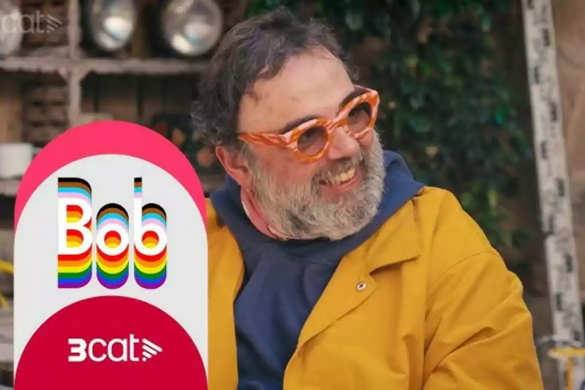 Bob Pop con gafas naranjas y barba sonríe mientras lleva una chaqueta amarilla en su programa Bob in translation, con un cartel que dice Bob Pop con gafas naranjas y barba sonríe mientras lleva una chaqueta amarilla en su programa Bob in translation, con un cartel que dice