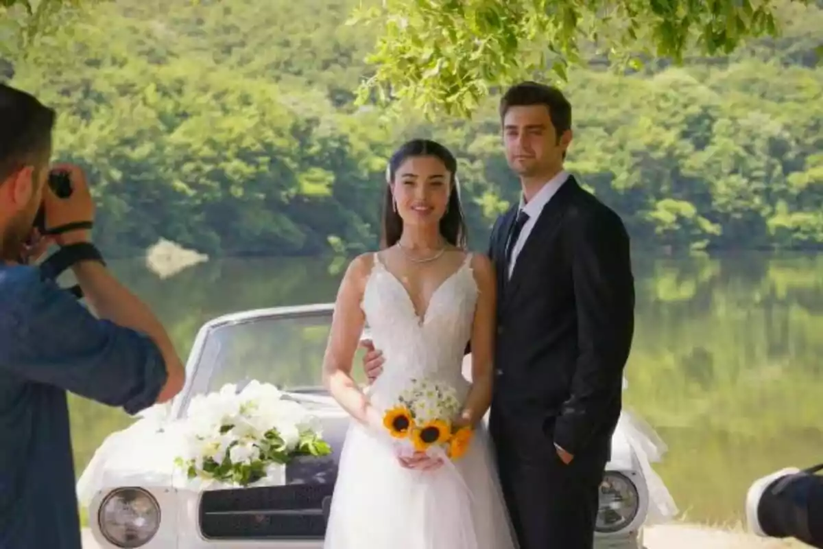 Asiye y Ömer de novios posando para una sesión de fotos junto a un automóvil clásico en un entorno natural con un lago y árboles al fondo en Hermanos. Asiye y Ömer de novios posando para una sesión de fotos junto a un automóvil clásico en un entorno natural con un lago y árboles al fondo en Hermanos.