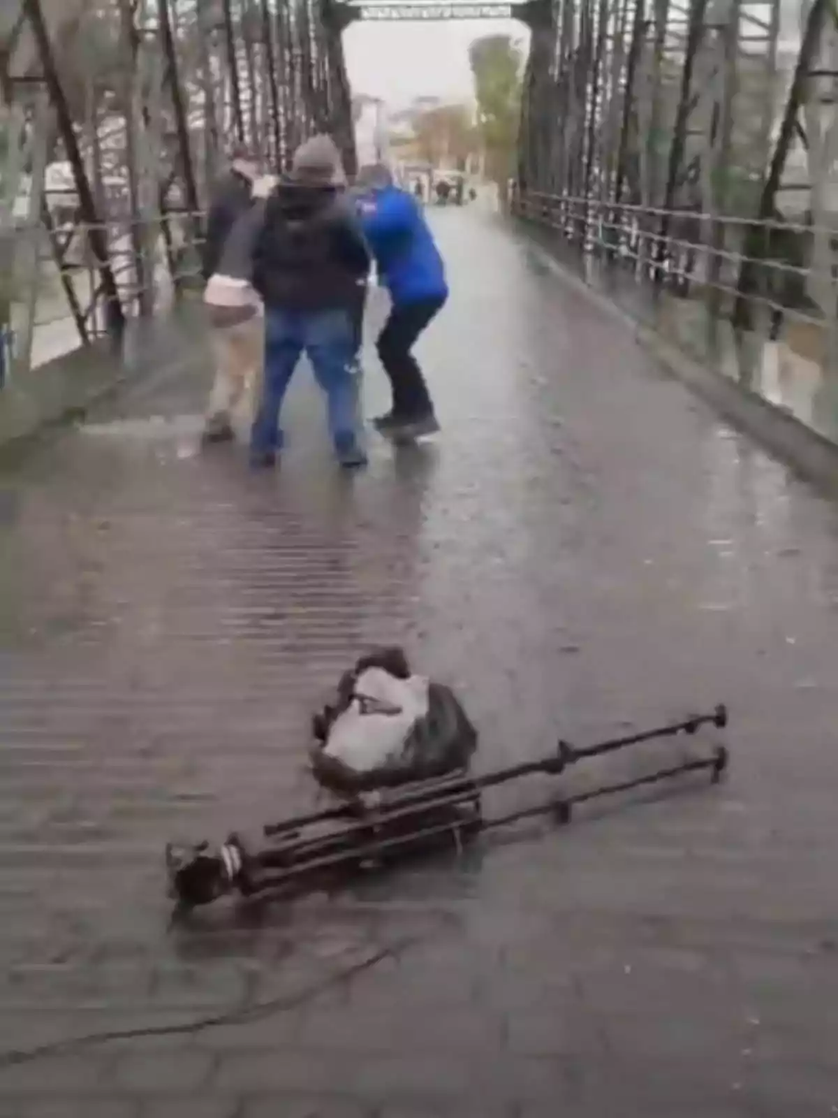 Tres personas están en un puente mojado, mientras un trípode y una bolsa están en el suelo. Tres personas están en un puente mojado, mientras un trípode y una bolsa están en el suelo.