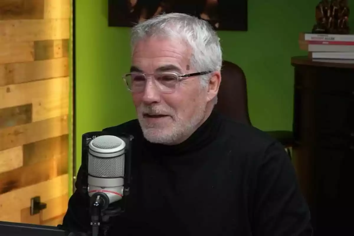 David Cantero de cabello canoso y barba con gafas y suéter negro hablando frente a un micrófono en un estudio con fondo verde. David Cantero de cabello canoso y barba con gafas y suéter negro hablando frente a un micrófono en un estudio con fondo verde.