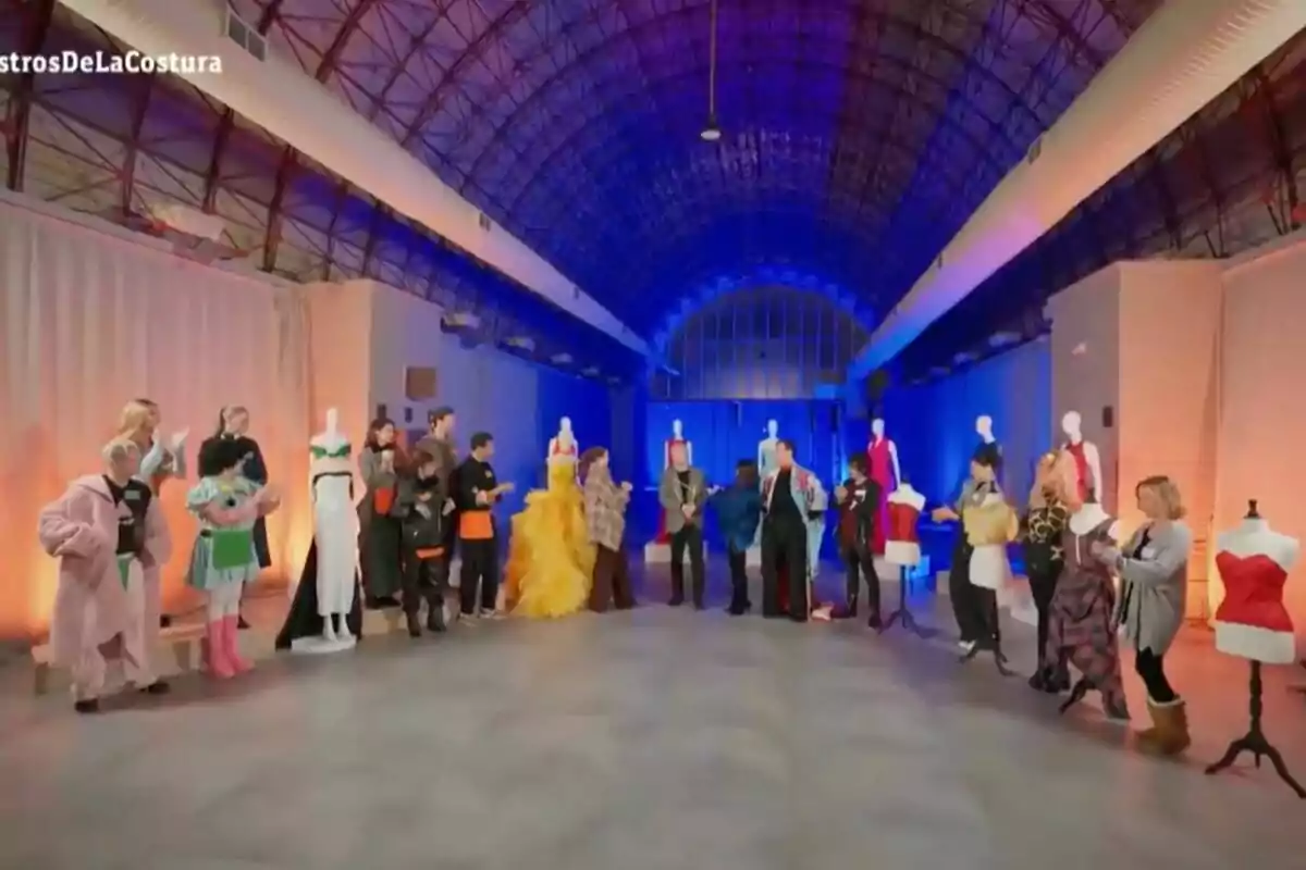 Un grupo de personas en un espacio amplio con techo abovedado, rodeados de maniquíes con vestidos coloridos y luces de colores en el fondo en 'Maestros de la Costura Celebrity'. Un grupo de personas en un espacio amplio con techo abovedado, rodeados de maniquíes con vestidos coloridos y luces de colores en el fondo en 'Maestros de la Costura Celebrity'.
