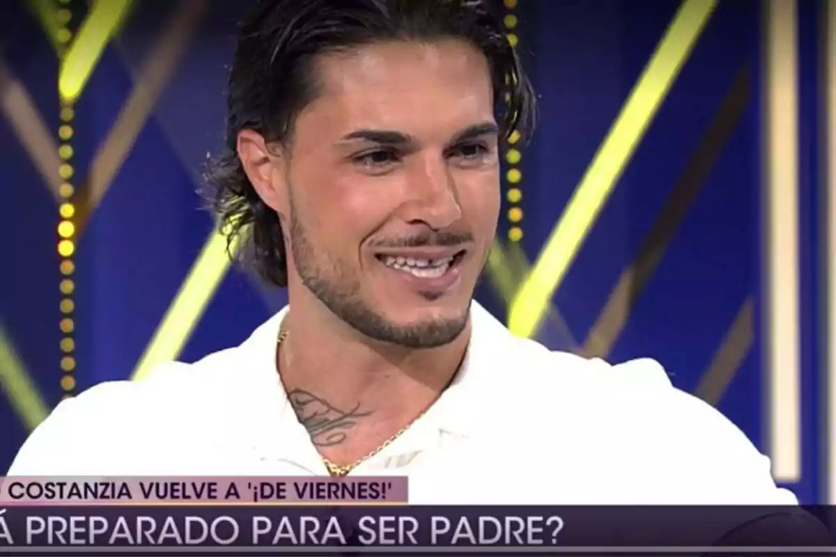 Carlo Costanzia con barba y cabello largo sonriendo en un programa de televisión con el texto Carlo Costanzia con barba y cabello largo sonriendo en un programa de televisión con el texto