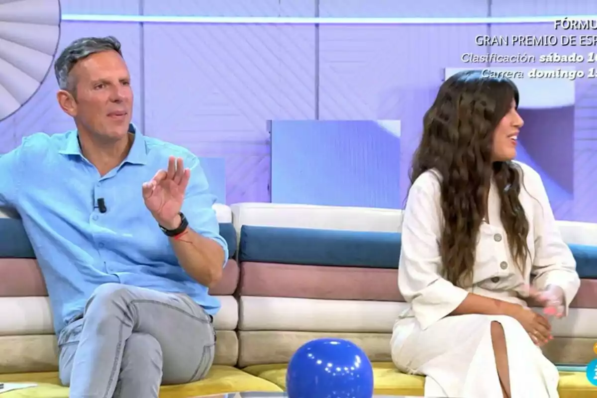 Dos personas sentadas en un sofá durante un programa de televisión, conversando y sonriendo. Dos personas sentadas en un sofá durante un programa de televisión, conversando y sonriendo.