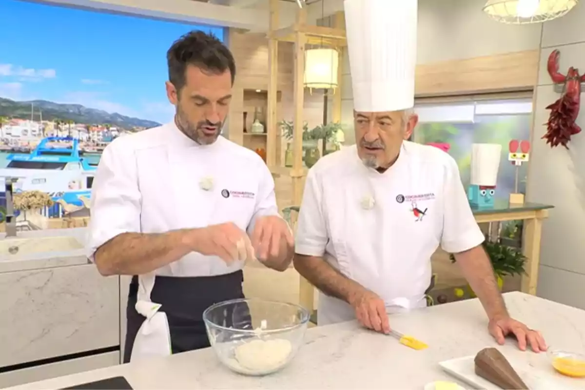 Karlos y Joseba Arguiñano con uniforme blanco preparan una receta en una cocina moderna mientras Joseba amasa en un bol de cristal y Karlos observa con atención Karlos y Joseba Arguiñano con uniforme blanco preparan una receta en una cocina moderna mientras Joseba amasa en un bol de cristal y Karlos observa con atención