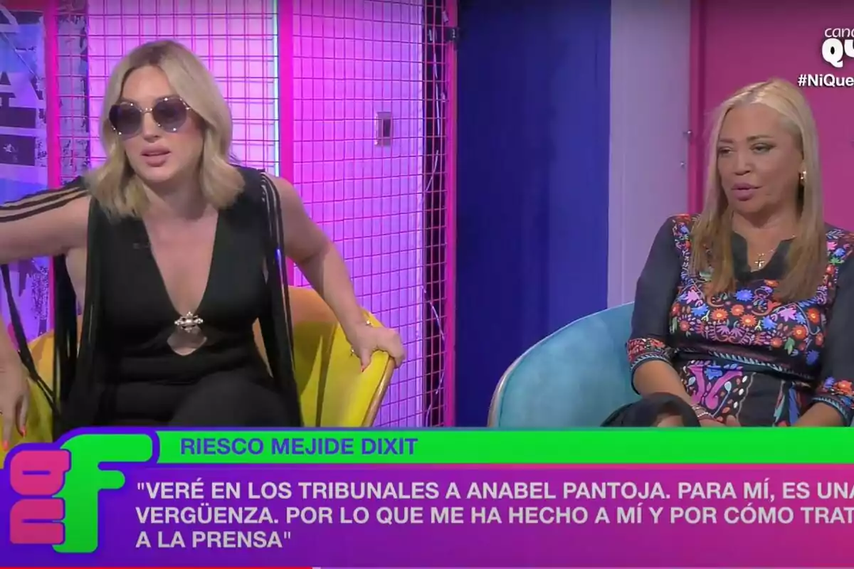 Dos mujeres sentadas en sillas coloridas en un set de televisión con iluminación rosa y azul, una de ellas lleva gafas de sol y un vestido negro, mientras que la otra viste un vestido con estampado floral, y en la parte inferior de la imagen hay un texto con una cita. Dos mujeres sentadas en sillas coloridas en un set de televisión con iluminación rosa y azul, una de ellas lleva gafas de sol y un vestido negro, mientras que la otra viste un vestido con estampado floral, y en la parte inferior de la imagen hay un texto con una cita.