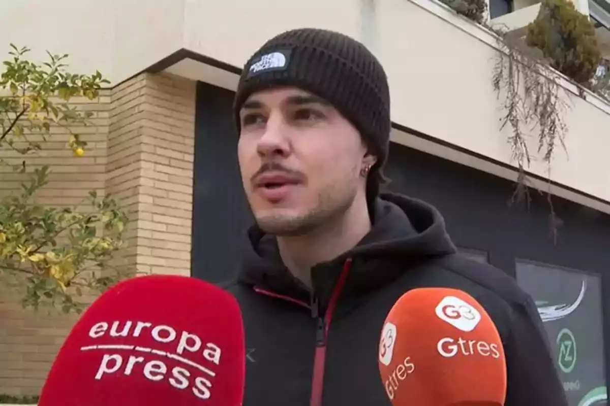 Carlo Costanzia con gorro negro y chaqueta oscura es entrevistado por varios medios de comunicación frente a un edificio. Carlo Costanzia con gorro negro y chaqueta oscura es entrevistado por varios medios de comunicación frente a un edificio.