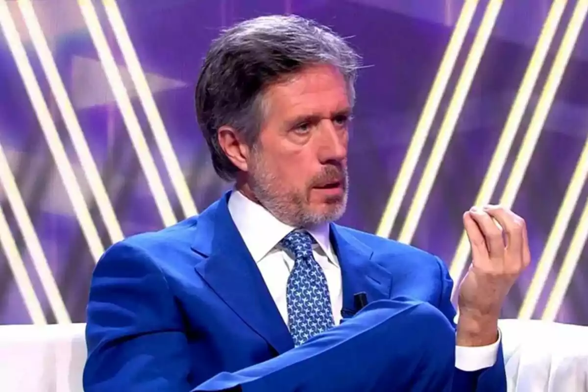 Carlo Costanzia con traje azul y corbata estampada está sentado en De Viernes con un fondo de luces diagonales. Carlo Costanzia con traje azul y corbata estampada está sentado en De Viernes con un fondo de luces diagonales.