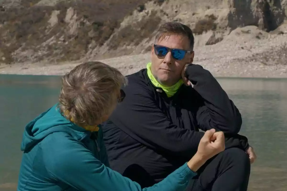 Jesús Calleja y Carlos Latre conversan al aire libre junto a un lago con montañas de fondo una de ellas lleva gafas de sol y ambas visten ropa deportiva en Universo Calleja. Jesús Calleja y Carlos Latre conversan al aire libre junto a un lago con montañas de fondo una de ellas lleva gafas de sol y ambas visten ropa deportiva en Universo Calleja.