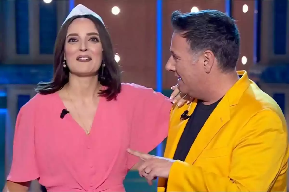 Carlos Latre y Leonor Lavado sonríen y conversan en Babylon Show, una mujer con vestido rosa y un hombre con chaqueta amarilla. Carlos Latre y Leonor Lavado sonríen y conversan en Babylon Show, una mujer con vestido rosa y un hombre con chaqueta amarilla.
