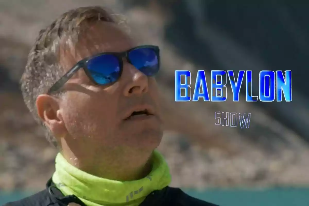 Carlos Latre con gafas de sol y bufanda verde claro en Universo Calleja mirando hacia arriba con el texto "Babylon Show" en letras azules.