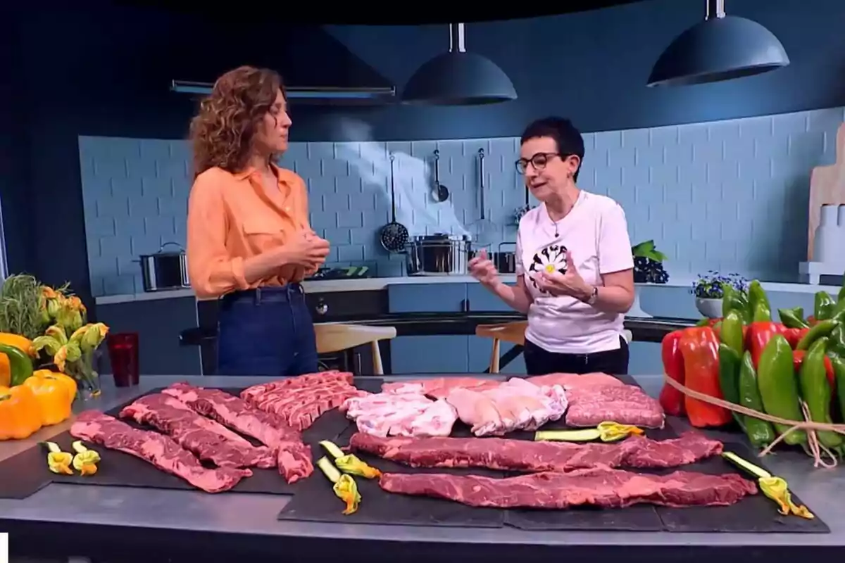 Helena García Meleroo i Carme Ruscalleda conversen en una cuina moderna amb una taula plena de diferents talls de carn i verdures fresques a Tot es Mou. Helena García Meleroo i Carme Ruscalleda conversen en una cuina moderna amb una taula plena de diferents talls de carn i verdures fresques a Tot es Mou.