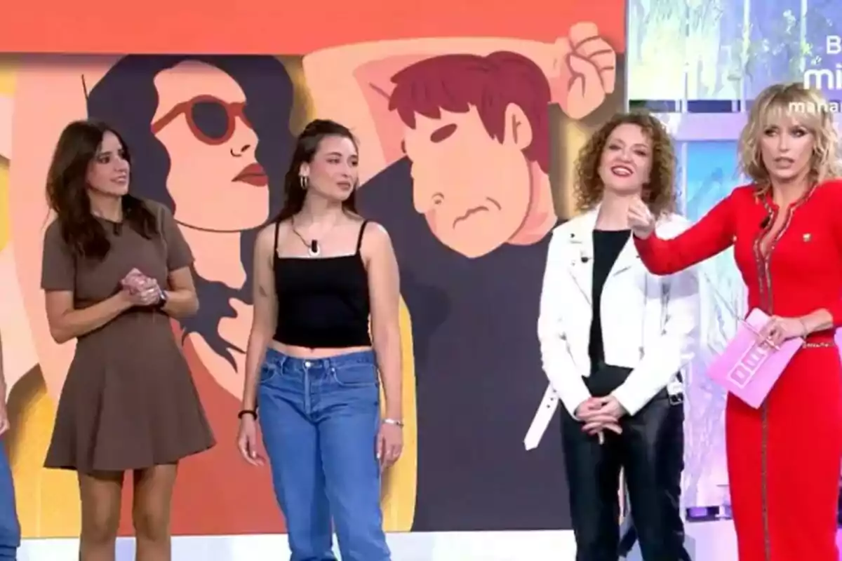 Un grupo de personas con Emma García y Carmen Alcayde está de pie frente a una pantalla que muestra una ilustración colorida en Fiesta. Un grupo de personas con Emma García y Carmen Alcayde está de pie frente a una pantalla que muestra una ilustración colorida en Fiesta.