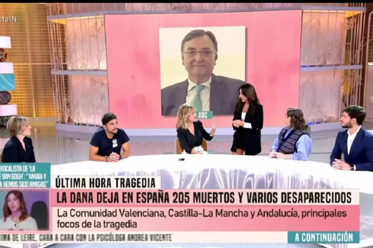 Un grupo de personas como Emma García y Carmen Alcayde está sentados en el plató de Fiesta discutiendo sobre una tragedia en España, con un gran retrato de un hombre en el fondo y un titular que informa sobre los efectos de la DANA en varias regiones. Un grupo de personas como Emma García y Carmen Alcayde está sentados en el plató de Fiesta discutiendo sobre una tragedia en España, con un gran retrato de un hombre en el fondo y un titular que informa sobre los efectos de la DANA en varias regiones.