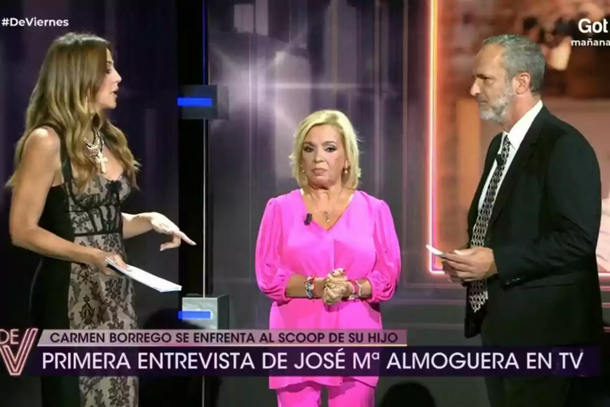 Tres personas están en el plató de De Viernes, Beatriz Archidona a la izquierda con un vestido negro, Carmen Borrego en el centro con un conjunto rosa y Santi Acosta a la derecha con traje y corbata, con un rótulo en la parte inferior que dice Tres personas están en el plató de De Viernes, Beatriz Archidona a la izquierda con un vestido negro, Carmen Borrego en el centro con un conjunto rosa y Santi Acosta a la derecha con traje y corbata, con un rótulo en la parte inferior que dice