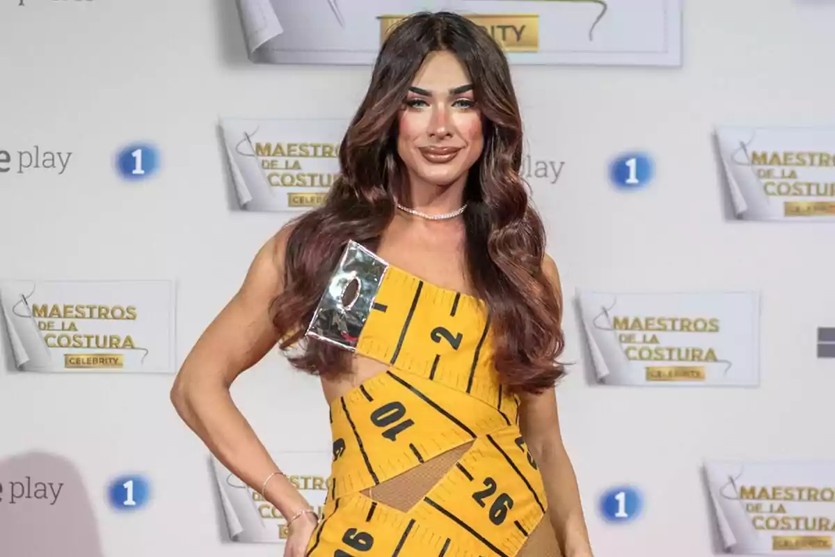 Carmen Farala amb un vestit groc amb disseny de cinta mètrica posa davant d'un fons amb logotips de Carmen Farala amb un vestit groc amb disseny de cinta mètrica posa davant d'un fons amb logotips de