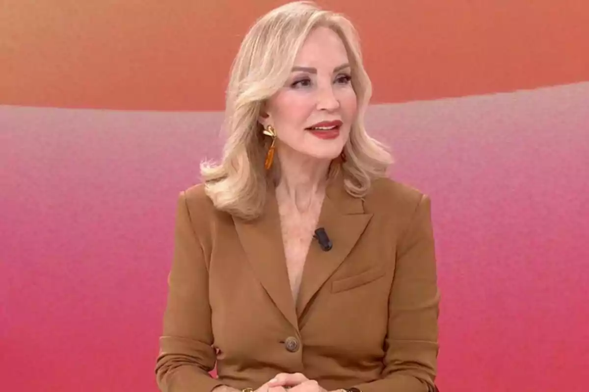 Carmen Lomana amb cabell ros i solt, vestida amb un vestit marró, està asseguda davant d'un fons degradat de tons rosats i taronges a 'Y ahora Sonsoles'.
