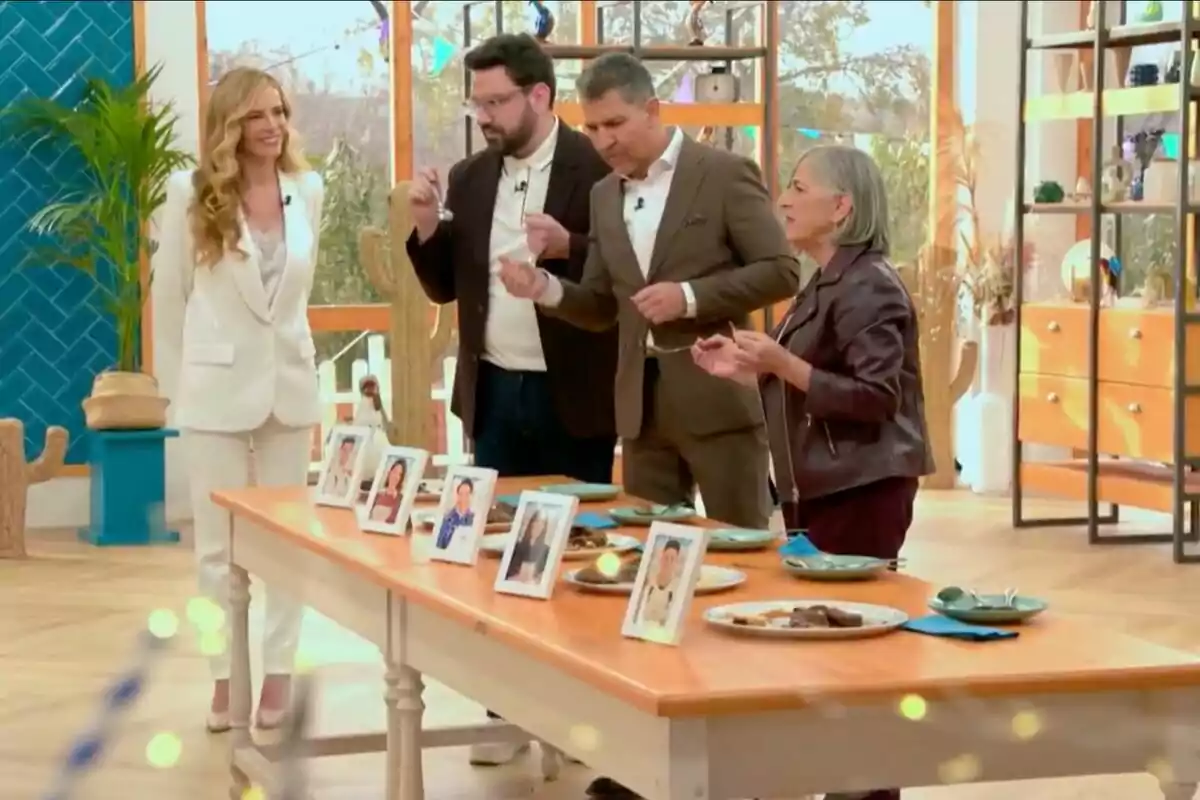 Jurado de 'Bake off: Famosos al horno' y Paula Vázquez está de pie alrededor de una mesa con platos y fotos en un ambiente interior decorado con plantas y estantes. Jurado de 'Bake off: Famosos al horno' y Paula Vázquez está de pie alrededor de una mesa con platos y fotos en un ambiente interior decorado con plantas y estantes.