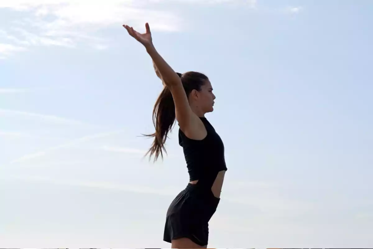 Celia Espanya con ropa deportiva negra levantando los brazos al cielo en un día soleado. Celia Espanya con ropa deportiva negra levantando los brazos al cielo en un día soleado.