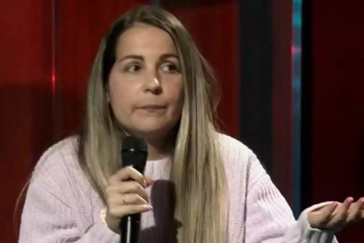 Una mujer con cabello largo y rubio sostiene un micrófono mientras parece estar hablando en un entorno con fondo rojo en La Revuelta. Una mujer con cabello largo y rubio sostiene un micrófono mientras parece estar hablando en un entorno con fondo rojo en La Revuelta.