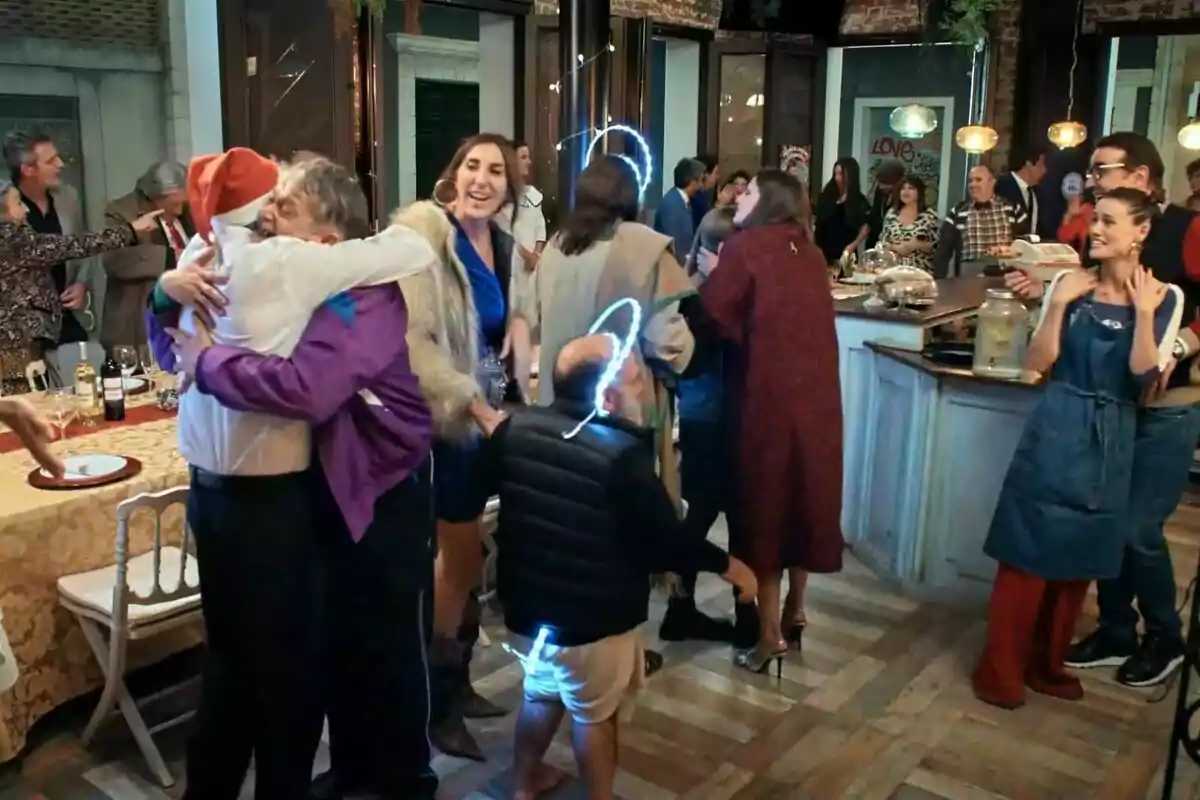 Un grupo de personas celebra en una fiesta, algunas se abrazan y otras conversan animadamente alrededor de una mesa decorada en La que se avecina.