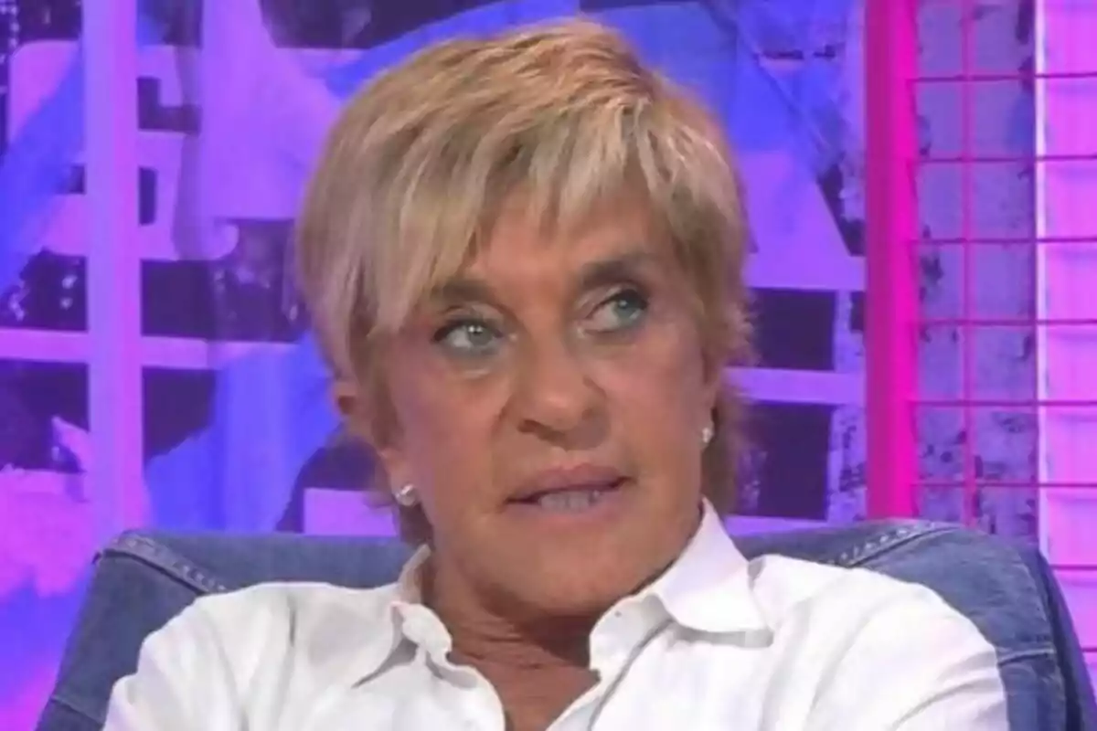 Una persona amb cabell curt ros i camisa blanca està asseguda en un entorn amb llums de colors. Una persona amb cabell curt ros i camisa blanca està asseguda en un entorn amb llums de colors.