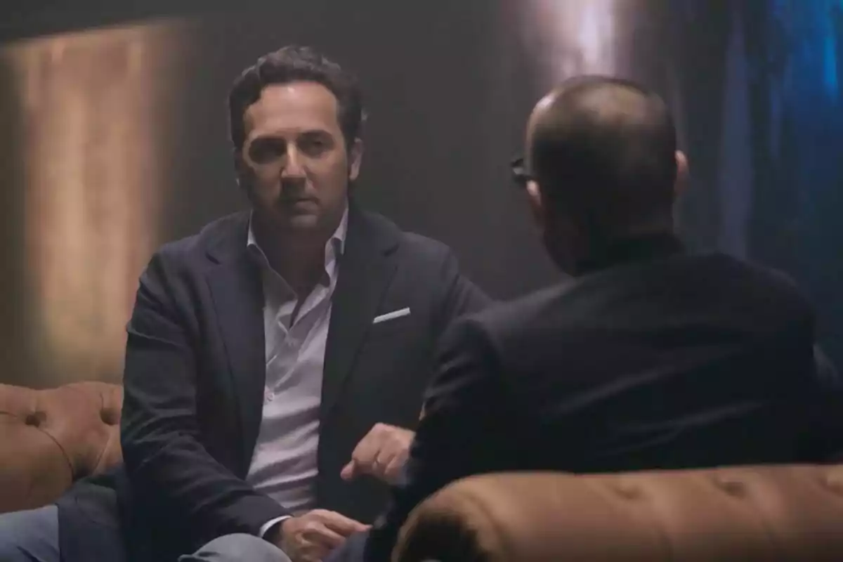 Risto Mejide e Iker Jiménez sentados en un sofá, uno de ellos de espaldas, en una conversación en un ambiente oscuro y elegante en 'Viajando con Chester'.