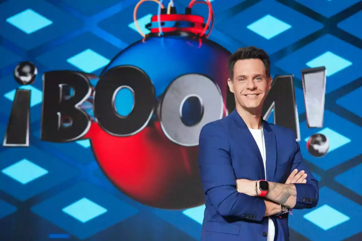 Christian Gálvez amb jaqueta blava i rellotge vermell somriu davant d'un fons amb el logo del programa Christian Gálvez amb jaqueta blava i rellotge vermell somriu davant d'un fons amb el logo del programa