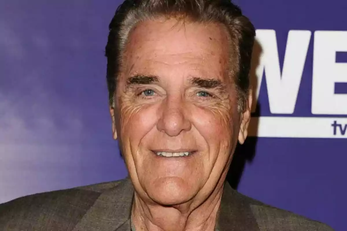 Chuck Woolery mayor con cabello canoso y ojos azules sonríe frente a un fondo morado. Chuck Woolery mayor con cabello canoso y ojos azules sonríe frente a un fondo morado.