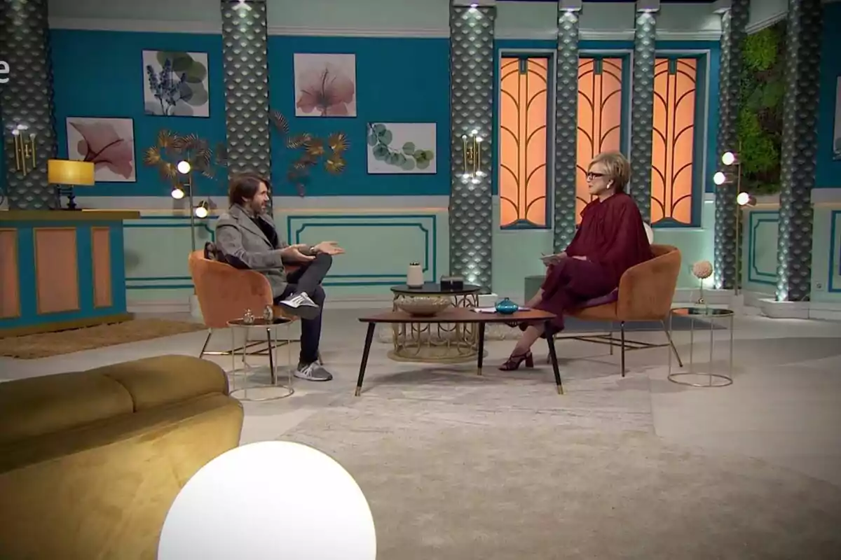 Manuel Velasco e Inés Ballester sentados en un set de televisión decorado con tonos azules y naranjas, conversando en un ambiente moderno y elegante en 'Cine de barrio'. Manuel Velasco e Inés Ballester sentados en un set de televisión decorado con tonos azules y naranjas, conversando en un ambiente moderno y elegante en 'Cine de barrio'.