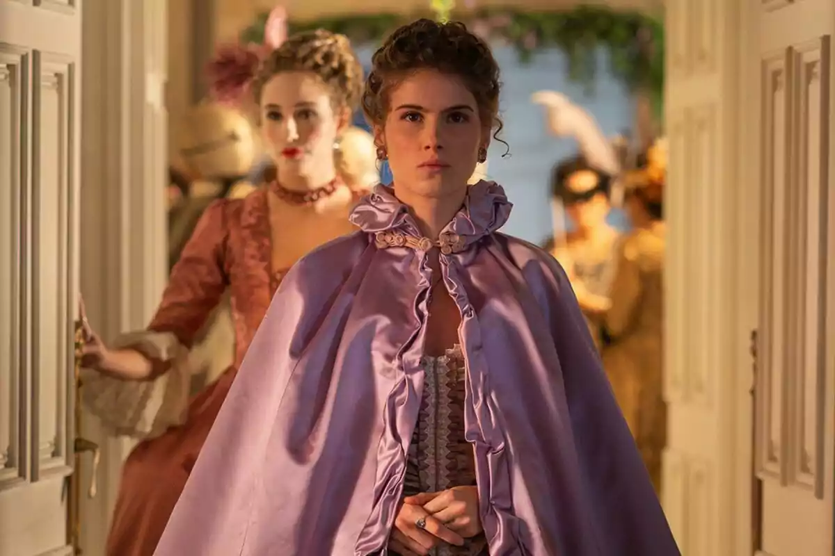 Claudia Oslé amb capa de setí lila està en primer pla mentre una altra dona amb vestit d'època està darrere en una habitació elegantment decorada a Valle Salvaje.