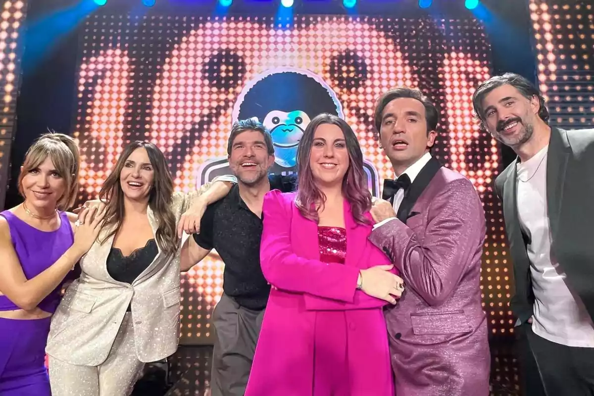 María Gómez, Melani Olivares, Nacho García, Carolina Iglesias, Miguel Lago i David Amor posant juntes en un escenari amb un fons il·luminat i colorit a El Club del Chiste. María Gómez, Melani Olivares, Nacho García, Carolina Iglesias, Miguel Lago i David Amor posant juntes en un escenari amb un fons il·luminat i colorit a El Club del Chiste.