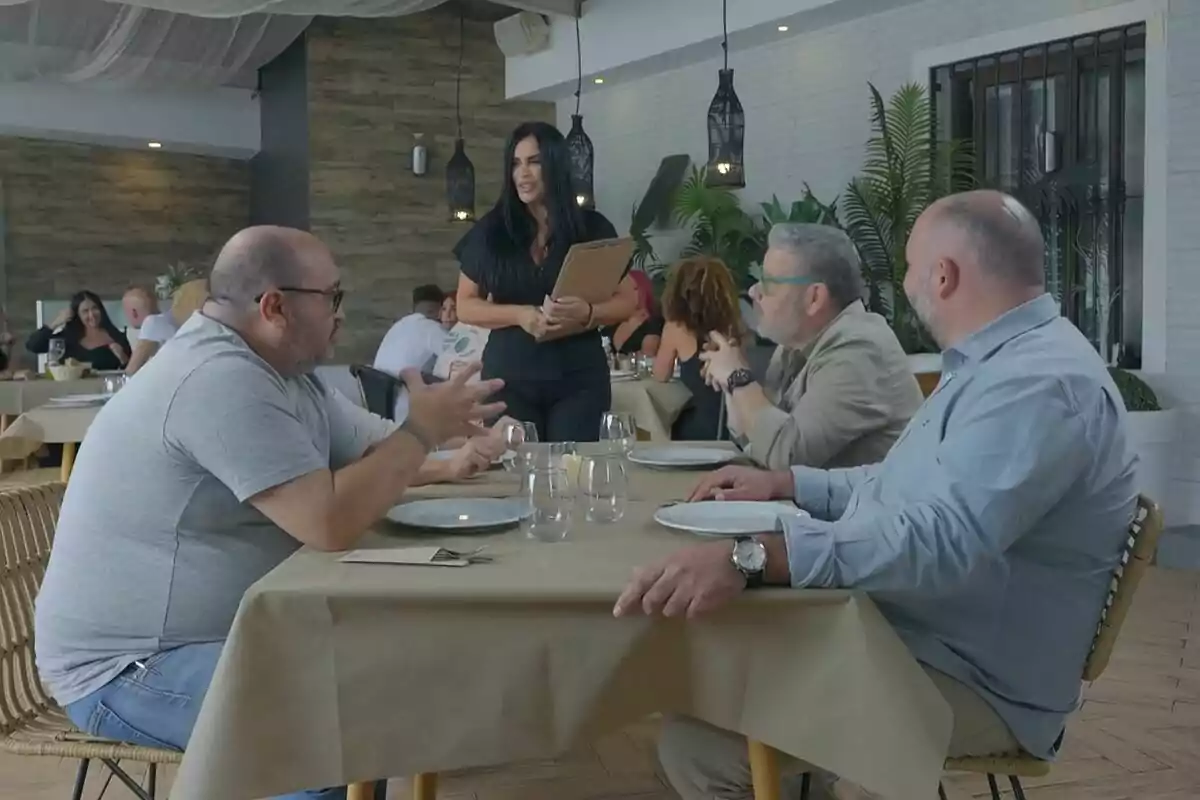 Un grup de persones juntament amb Alberto Chicote està assegut a una taula de restaurant mentre una cambrera pren la seva comanda a Batalla de Restaurants. Un grup de persones juntament amb Alberto Chicote està assegut a una taula de restaurant mentre una cambrera pren la seva comanda a Batalla de Restaurants.