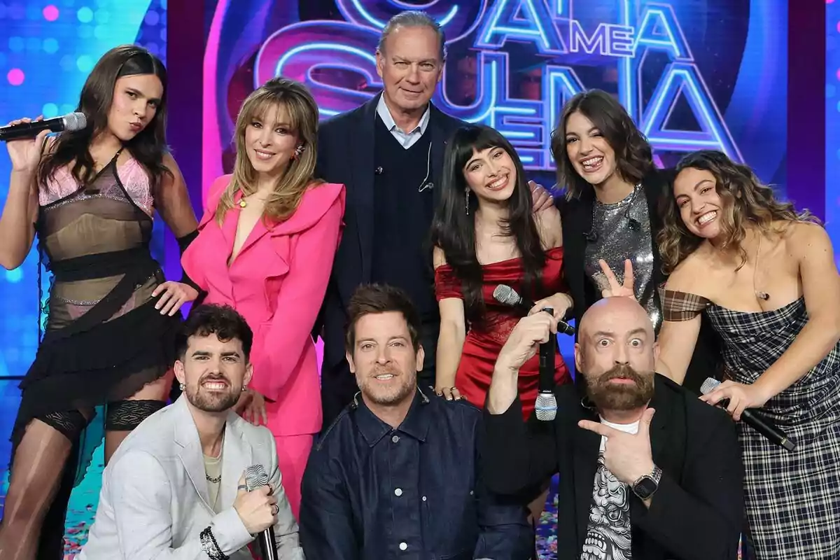 Un grup de persones format per Bertín Osborne, Ana Guerra, Manu Baqueiro, Gisela, Goyo Jiménez, Yenesi, Esperansa Grasia, Melani García i Mikel Herzog Jr. posant juntes al plató de Tu Cara Me Suena, algunes sostenint micròfons i somrient a la càmera, amb un fons acolorit i un rètol que sembla ser part del programa.