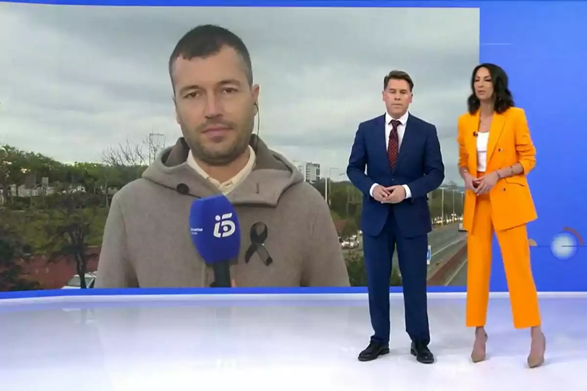 Tres personas en Informativos Telecinco, Bricio Segovia y Laila Martínez de pie y una en una pantalla detrás, con un micrófono azul.