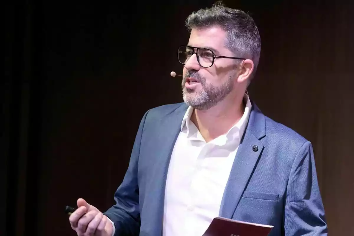 Cristian Trepat amb ulleres i barba fent servir un micròfon de diadema mentre fa una presentació de 3Cat