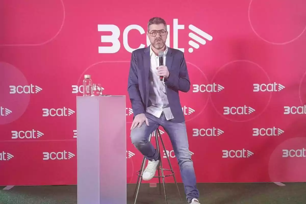 Cristian Trepat amb ulleres i barba està assegut en un tamboret sostenint un micròfon davant d'un fons vermell amb el logotip de 3cat repetit. Cristian Trepat amb ulleres i barba està assegut en un tamboret sostenint un micròfon davant d'un fons vermell amb el logotip de 3cat repetit.