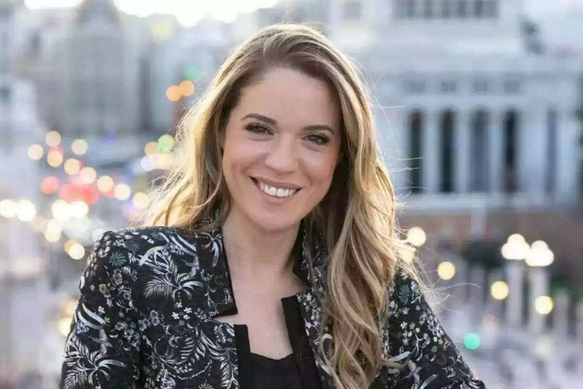 Cristina Lasvignes joven de cabello rubio y largo sonriendo al aire libre con fondo urbano desenfocado y luces de la ciudad al atardecer