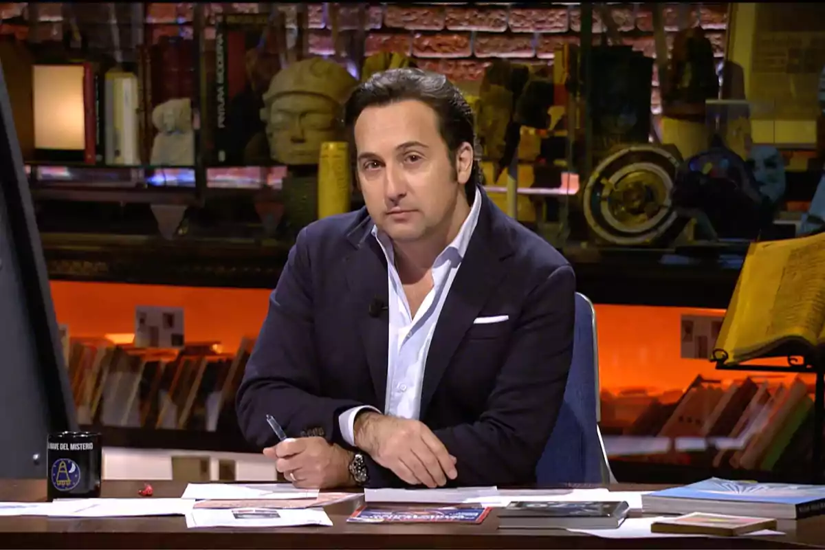 Iker Jiménez sentado en un escritorio con libros y papeles, en un ambiente de estudio con estanterías y objetos decorativos al fondo. Captura de 'Cuarto Milenio'