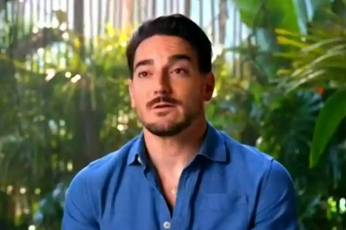 Damián Quintero con barba y camisa azul está hablando frente a un fondo de vegetación en Supervivientes.