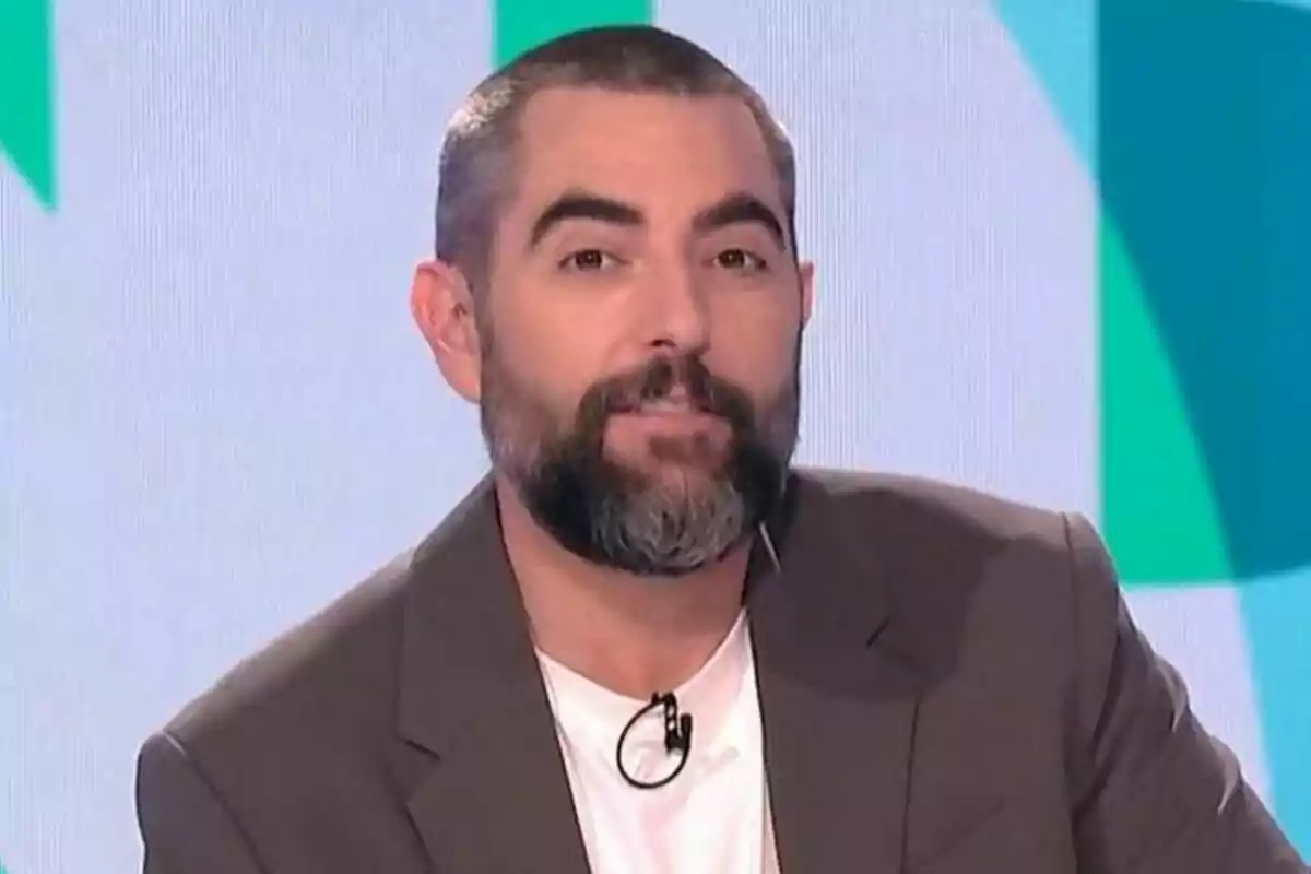 Dani Mateo con barba y cabello corto lleva un traje marrón y una camiseta blanca mientras está en Zapeando.