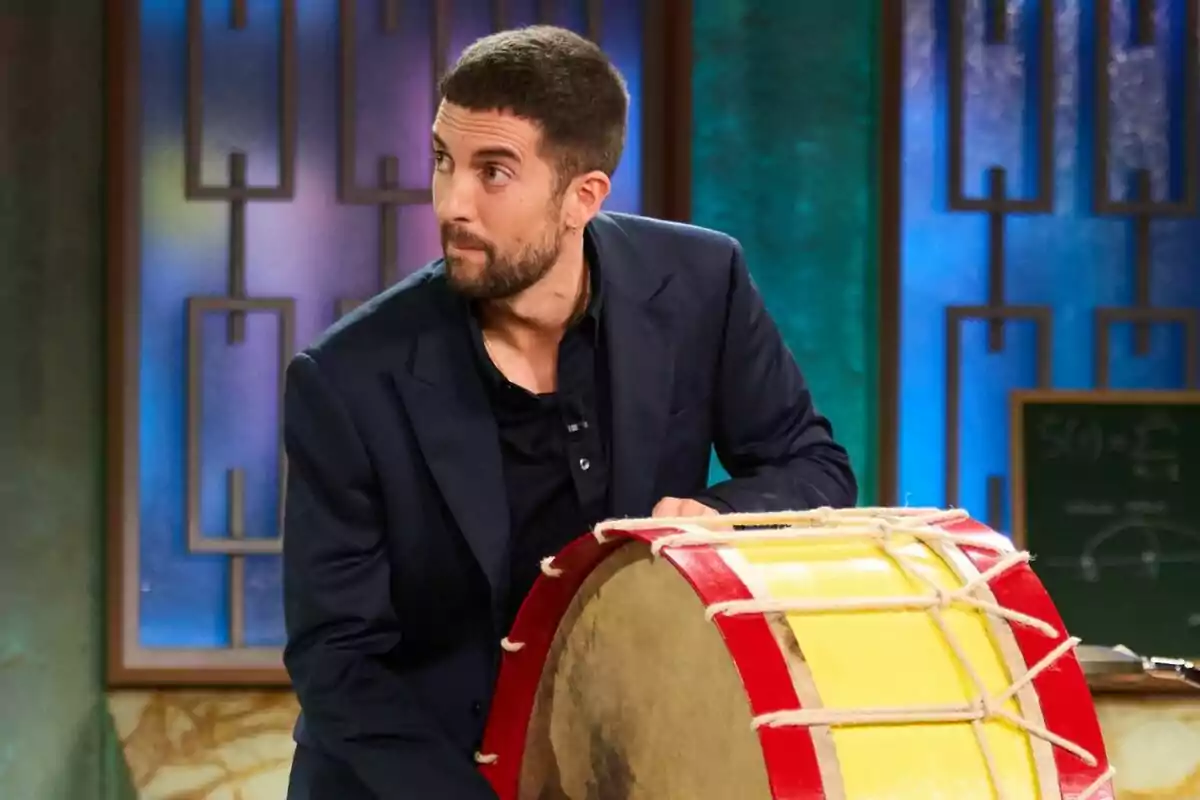 David Broncano amb barba i cabells curts tocant un tambor gran en un escenari amb fons colorit a La Revuelta. David Broncano amb barba i cabells curts tocant un tambor gran en un escenari amb fons colorit a La Revuelta.