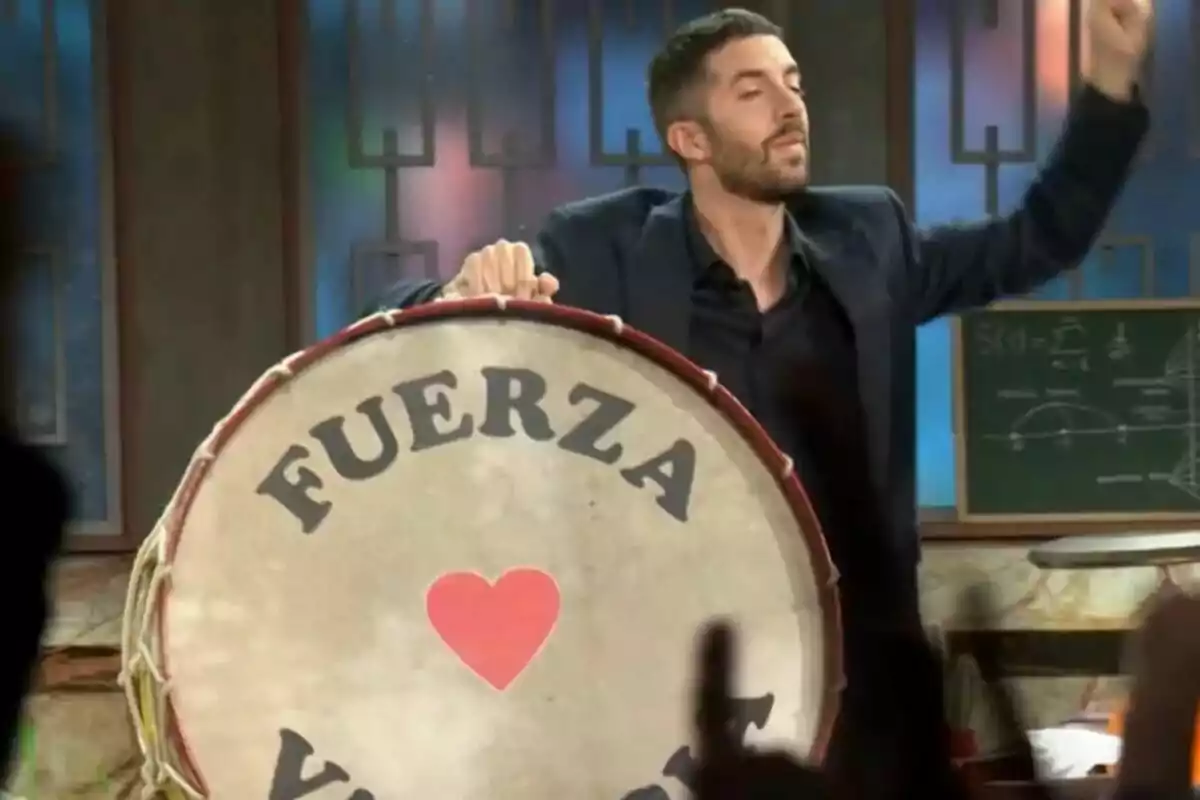 David Broncano con barba toca un bombo grande que tiene la palabra David Broncano con barba toca un bombo grande que tiene la palabra