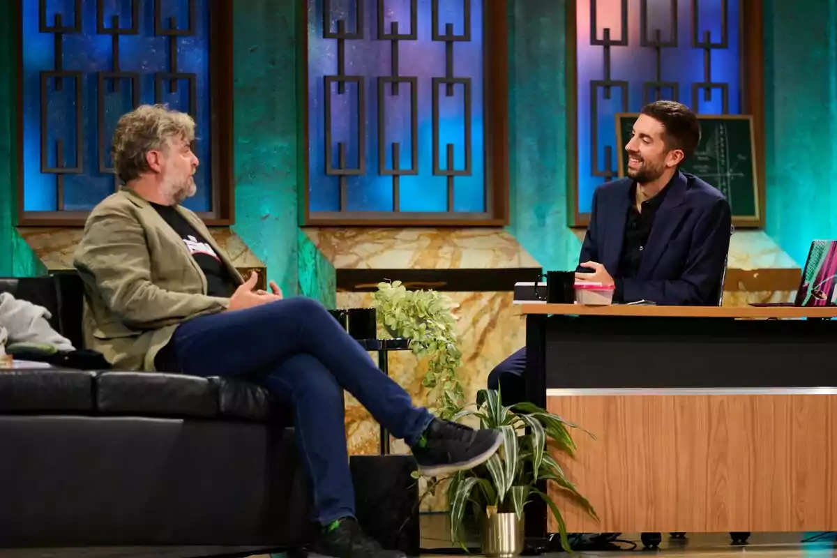 David Broncano i Raúl Cimas conversen a La Revuelta, un assegut en un sofà i l'altre darrere d'un escriptori, amb una decoració de fons que inclou finestres amb vitralls i plantes. David Broncano i Raúl Cimas conversen a La Revuelta, un assegut en un sofà i l'altre darrere d'un escriptori, amb una decoració de fons que inclou finestres amb vitralls i plantes.