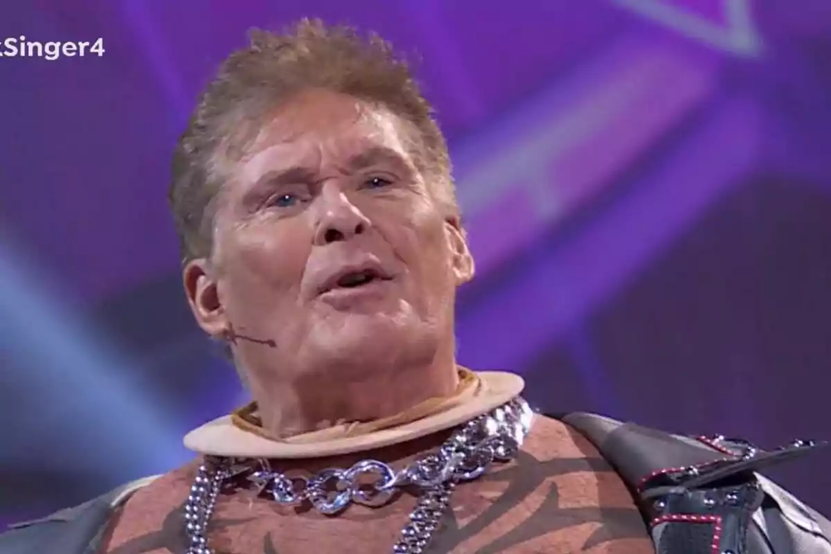 David Hasselhoff con un traje llamativo y un micrófono en la mejilla sobre un fondo púrpura en Mask Singer. David Hasselhoff con un traje llamativo y un micrófono en la mejilla sobre un fondo púrpura en Mask Singer.