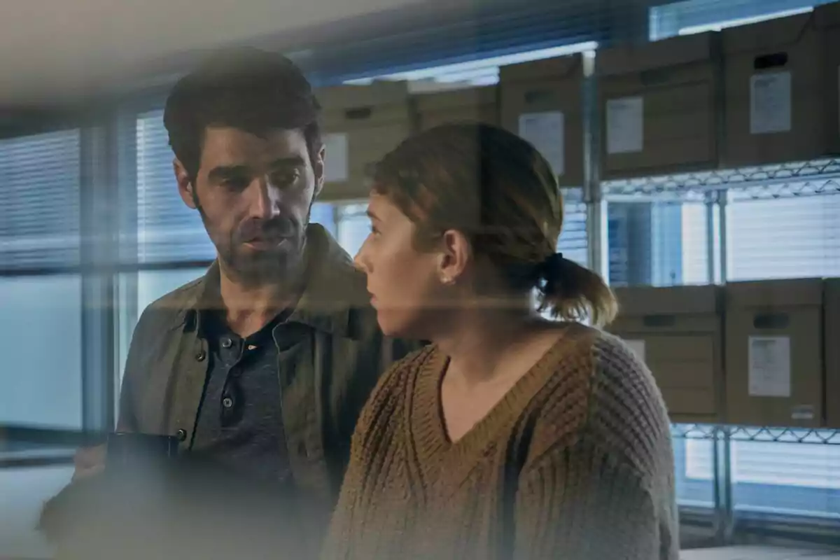 Fotografia de David Verdaguer i Ángela Cervantes conversant en una oficina amb caixes d'arxiu al fons a la sèrie El Mal Invisible