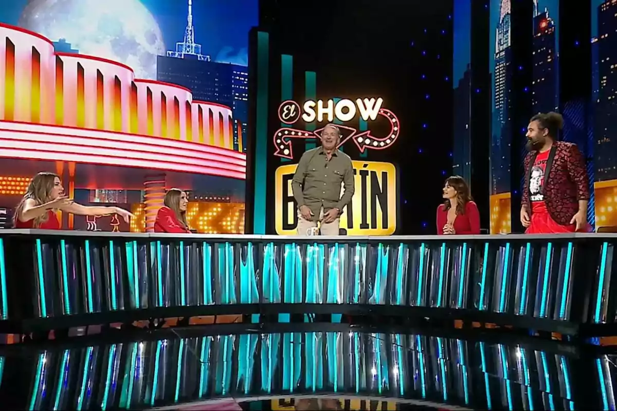 Un grupo de personas como Bertín Osborne, Susana Saborido o el Sevilla participa en El Show de Bertín con un escenario iluminado y un fondo que simula un paisaje urbano nocturno. Un grupo de personas como Bertín Osborne, Susana Saborido o el Sevilla participa en El Show de Bertín con un escenario iluminado y un fondo que simula un paisaje urbano nocturno.