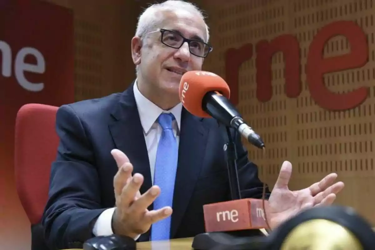 Diumenge Álvarez amb ulleres i vestit parla en un micròfon en un estudi de ràdio.