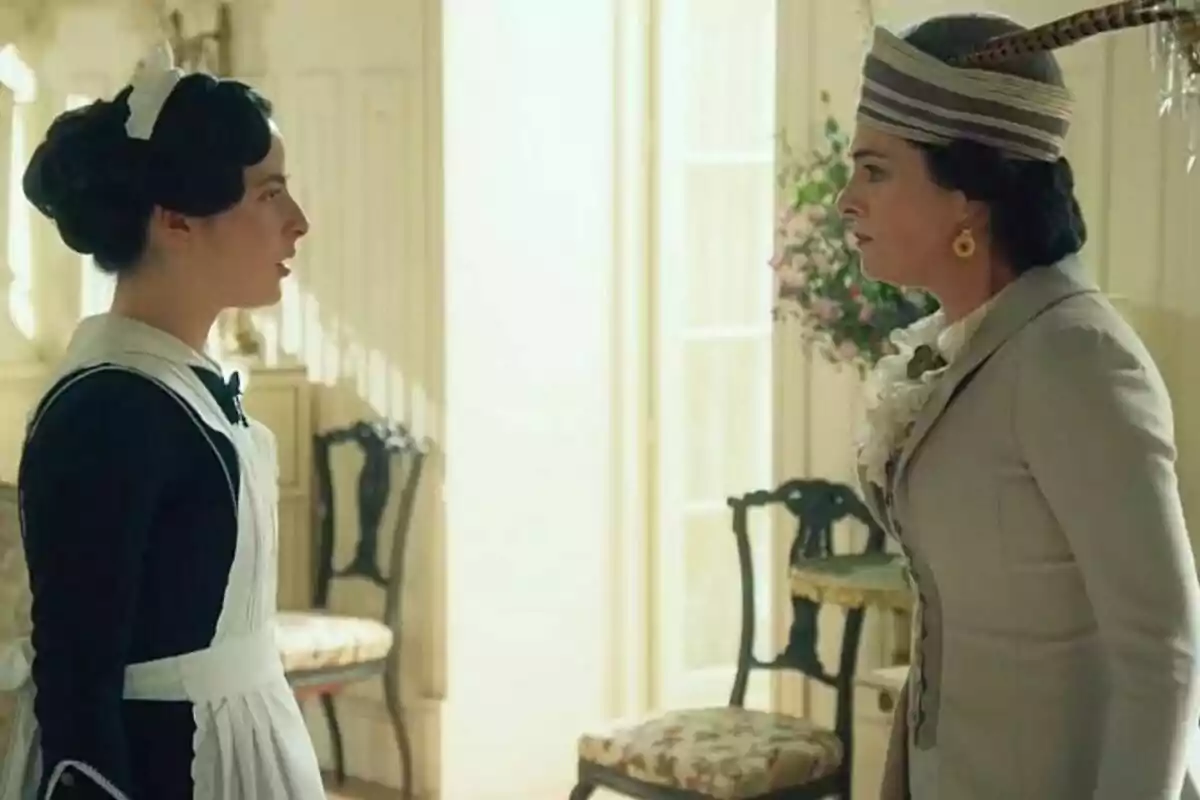 Rocío Muñoz-Cobo y Ángela Echániz vestidas con ropa de época se enfrentan en una habitación iluminada por la luz del día en La Promesa. Rocío Muñoz-Cobo y Ángela Echániz vestidas con ropa de época se enfrentan en una habitación iluminada por la luz del día en La Promesa.