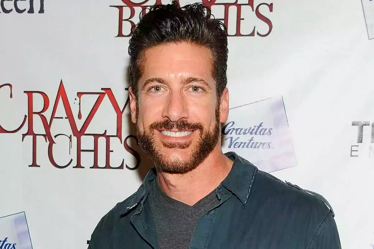 Eduardo Xol con barba y cabello oscuro sonriendo frente a un fondo con logotipos y texto. Eduardo Xol con barba y cabello oscuro sonriendo frente a un fondo con logotipos y texto.