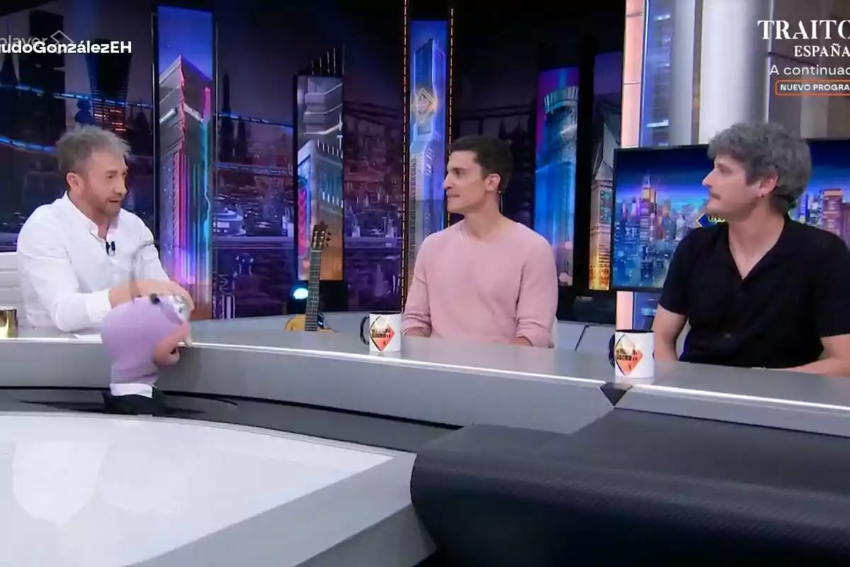 Pablo Motos, Álex González i Antonio Pagudo conversen a 'El Hormiguero', un plató modern amb una titella morada sobre la taula i tasses blanques davant seu. Pablo Motos, Álex González i Antonio Pagudo conversen a 'El Hormiguero', un plató modern amb una titella morada sobre la taula i tasses blanques davant seu.